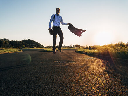 Businessman jumping on rural road - KNSF00797