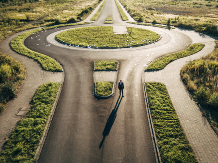 Businessman standing at roundabout with scattered papers behind - KNSF00801