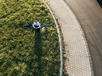 Businessman sitting next to laptop on traffic island in roundabout - KNSF00805