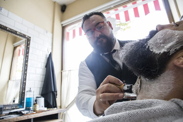 Barbier stellt Rasierschaum in den Bart eines Mannes - ABZF01670