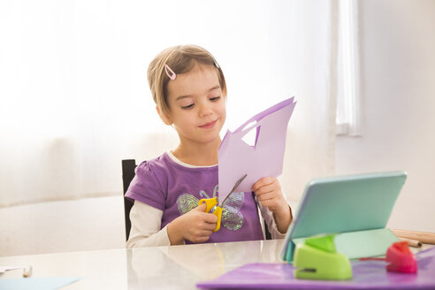 Little girl tinlering at home, cutting paper with online instructions - LVF05738