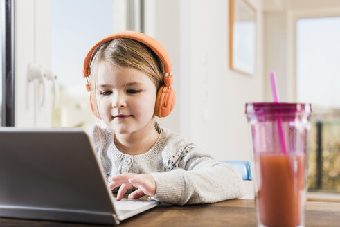 Kleines Mädchen sitzt zu Hause mit Laptop und Kopfhörern - UUF09530