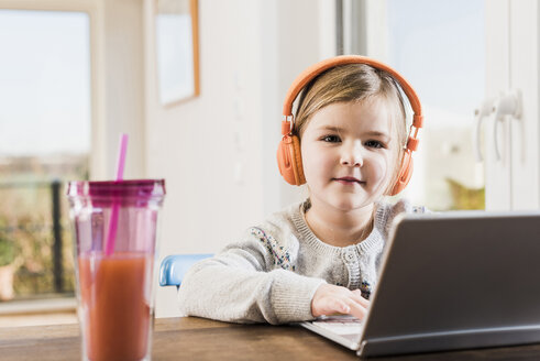 Kleines Mädchen sitzt zu Hause mit Laptop und Kopfhörern - UUF09531