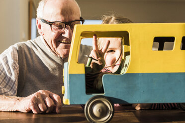 Großvater und Enkelin bauen einen Spielzeugbus zusammen, das Mädchen macht ein Siegeszeichen - UUF09551