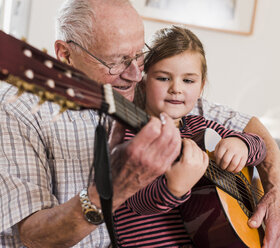 Grandfather and granddaughter playing together guitar - UUF09556
