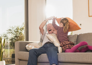 Großvater und Enkelin bei einer Kissenschlacht auf der Couch - UUF09558