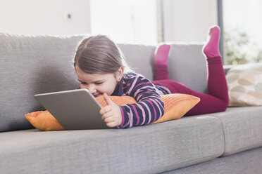 Kleines Mädchen mit digitalem Tablet, auf der Couch liegend - UUF09577