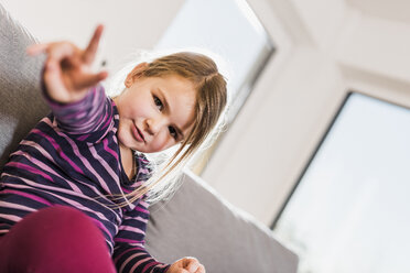 Kleines Mädchen sitzt auf der Couch und macht ein Siegeszeichen - UUF09579