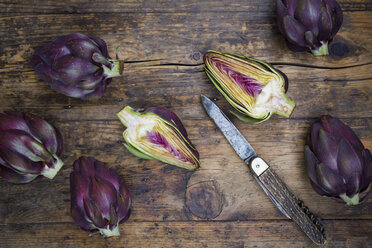 Sliced and whole purple organic artichokes and a pocket knife on dark wood - LVF05745