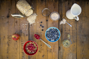 Schüssel Overnight Oats mit Heidelbeeren und Schüssel Granola mit Granatapfelkernen und rotem Apfel auf Holz - LVF05756