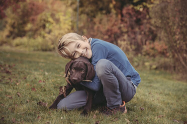 Junge, der einen Labrador Retriever im Garten umarmt - MFF03398