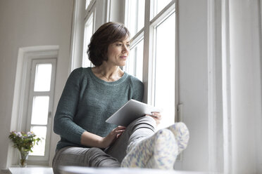 Woman with tablet looking out of window - RBF05342