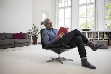 Älterer Mann sitzt zu Hause im Stuhl und liest ein Buch - RBF05375