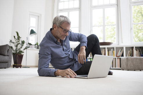 Älterer Mann zu Hause auf dem Boden liegend mit Laptop - RBF05376