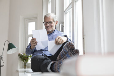 Älterer Mann sitzt zu Hause am Fenster und liest Dokumente - RBF05383
