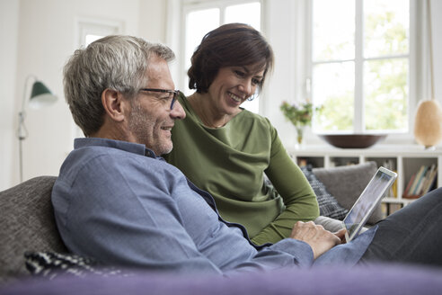 Lächelndes reifes Paar zu Hause auf dem Sofa, das sich ein Tablet teilt - RBF05385