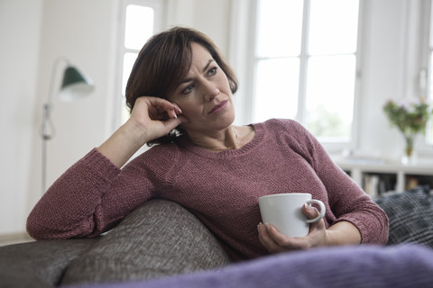 Frau zu Hause auf dem Sofa sitzend mit Tasse, lizenzfreies Stockfoto