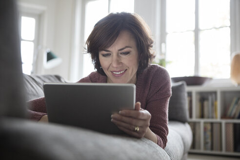 Frau zu Hause auf dem Sofa liegend mit Tablet - RBF05404