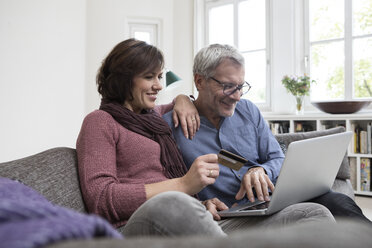 Lächelndes reifes Paar zu Hause auf dem Sofa beim Online-Shopping - RBF05406