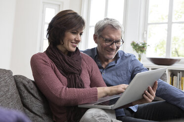 Lächelndes reifes Paar zu Hause auf dem Sofa mit Laptop - RBF05407