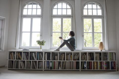 Frau zu Hause schaut aus dem Fenster, lizenzfreies Stockfoto