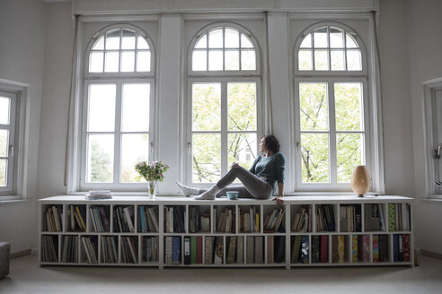 Frau zu Hause schaut aus dem Fenster - RBF05414