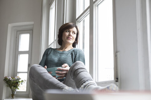 Frau zu Hause schaut aus dem Fenster - RBF05416