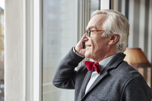 Lächelnder älterer Mann am Telefon am Fenster - RHF01703