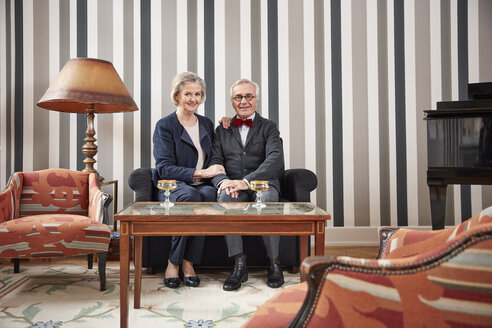 Lächelndes älteres Ehepaar sitzt mit Sektgläsern auf dem Sofa - RHF01711