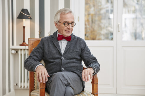 Älterer Mann sitzt auf einem Stuhl und schaut auf eine Smartwatch - RHF01715