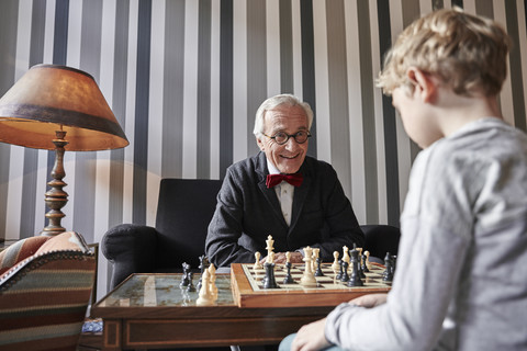 Grandfather and grandson playing chess in living room stock photo