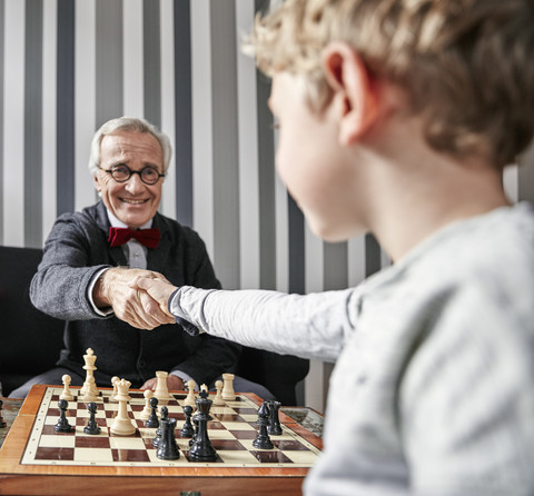 Großvater und Enkel schütteln sich die Hände über dem Schachbrett, lizenzfreies Stockfoto