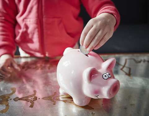 Mädchen legt Münze in Sparschwein, lizenzfreies Stockfoto