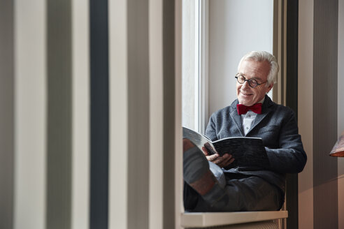 Älterer Mann sitzt auf der Fensterbank und liest eine Zeitschrift - RHF01743