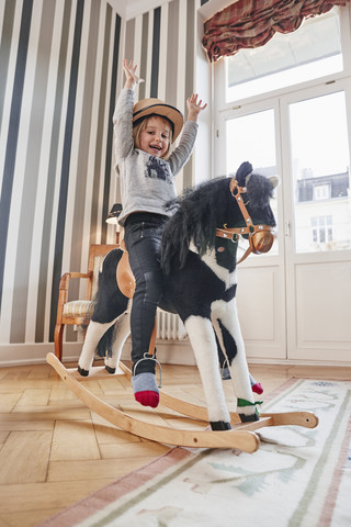 Glückliches Mädchen posiert auf einem Schaukelpferd, lizenzfreies Stockfoto