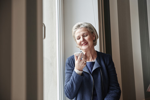 Ältere Frau benutzt Handy am Fenster, lizenzfreies Stockfoto
