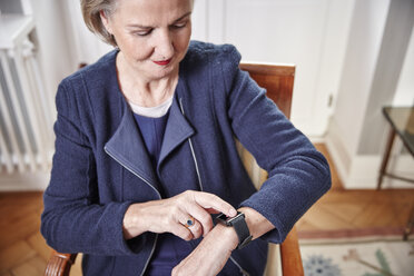 Ältere Frau sitzt auf einem Stuhl und schaut auf eine Smartwatch - RHF01769