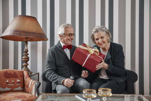 Glückliches älteres Paar sitzt mit Geschenk auf der Couch - RHF01781