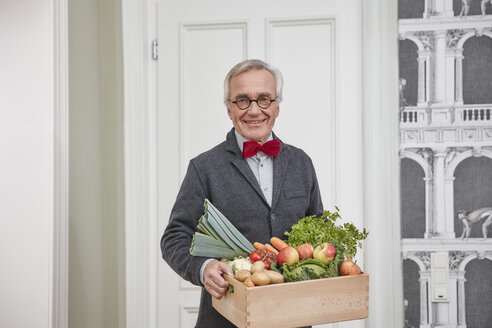 Porträt eines lächelnden älteren Mannes, der eine Kiste mit Produkten hält - RHF01782