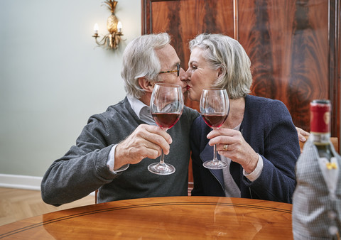 Senior couple holding red wine glasses kissing stock photo