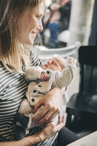 Lächelnde Mutter hält ihr schlafendes Baby in einem Cafe, lizenzfreies Stockfoto