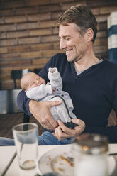 Lächelnder reifer Vater hält sein schlafendes Baby in einem Cafe - MFF03413