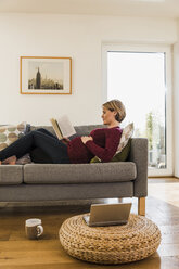 Pregnant woman on couch reading book - UUF09581