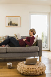 Schwangere Frau auf der Couch, die ein Buch liest - UUF09581