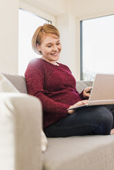 Smiling pregnant woman on couch shopping online - UUF09590