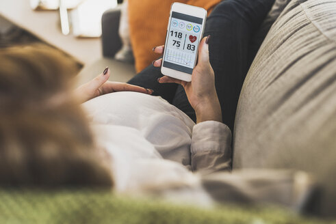 Pregnant woman on couch using smartphone checking health data - UUF09595