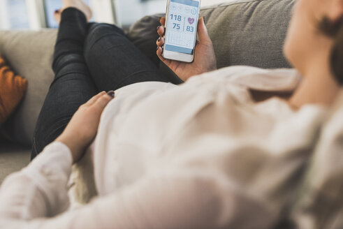 Schwangere Frau auf der Couch, die mit ihrem Smartphone Gesundheitsdaten überprüft - UUF09596