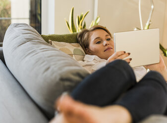 Junge Frau auf Couch liegend mit Tablet - UUF09598