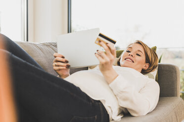 Lächelnde schwangere Frau auf Couch beim Online-Shopping - UUF09600