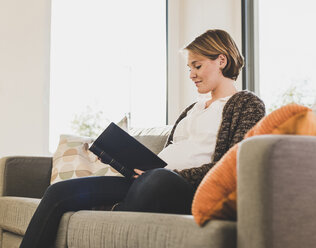 Pregnant woman on couch reading book - UUF09601